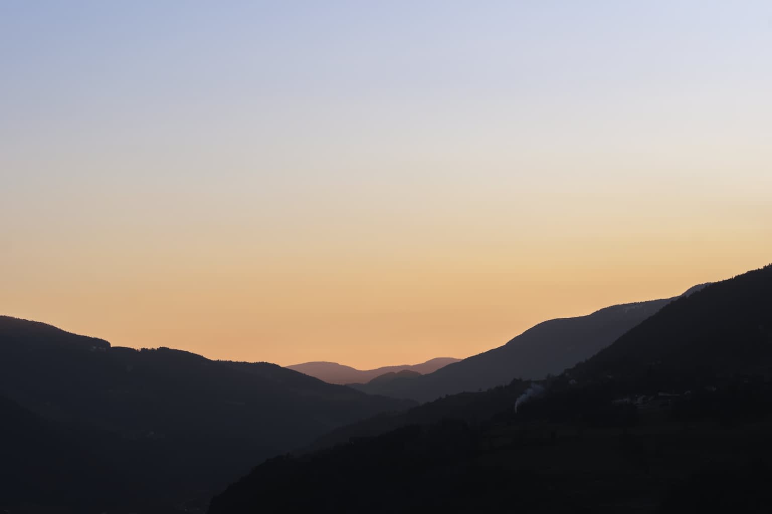 Sunset over the city Brixen in the Alps with cool blue reaching from the top and bottom of the image into the still-warm middle where layers of mountains overlap into the distance