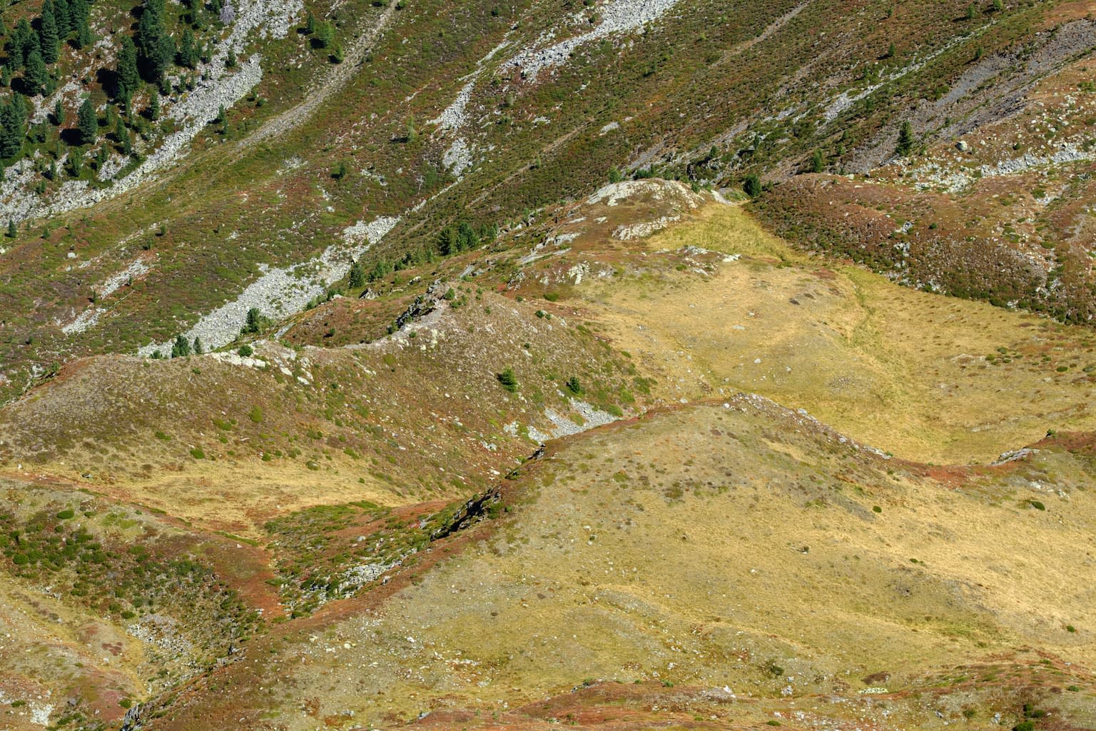 Early autumn colors of yellow and orange covering a hilly, mountainous region with rocks and a few green trees.