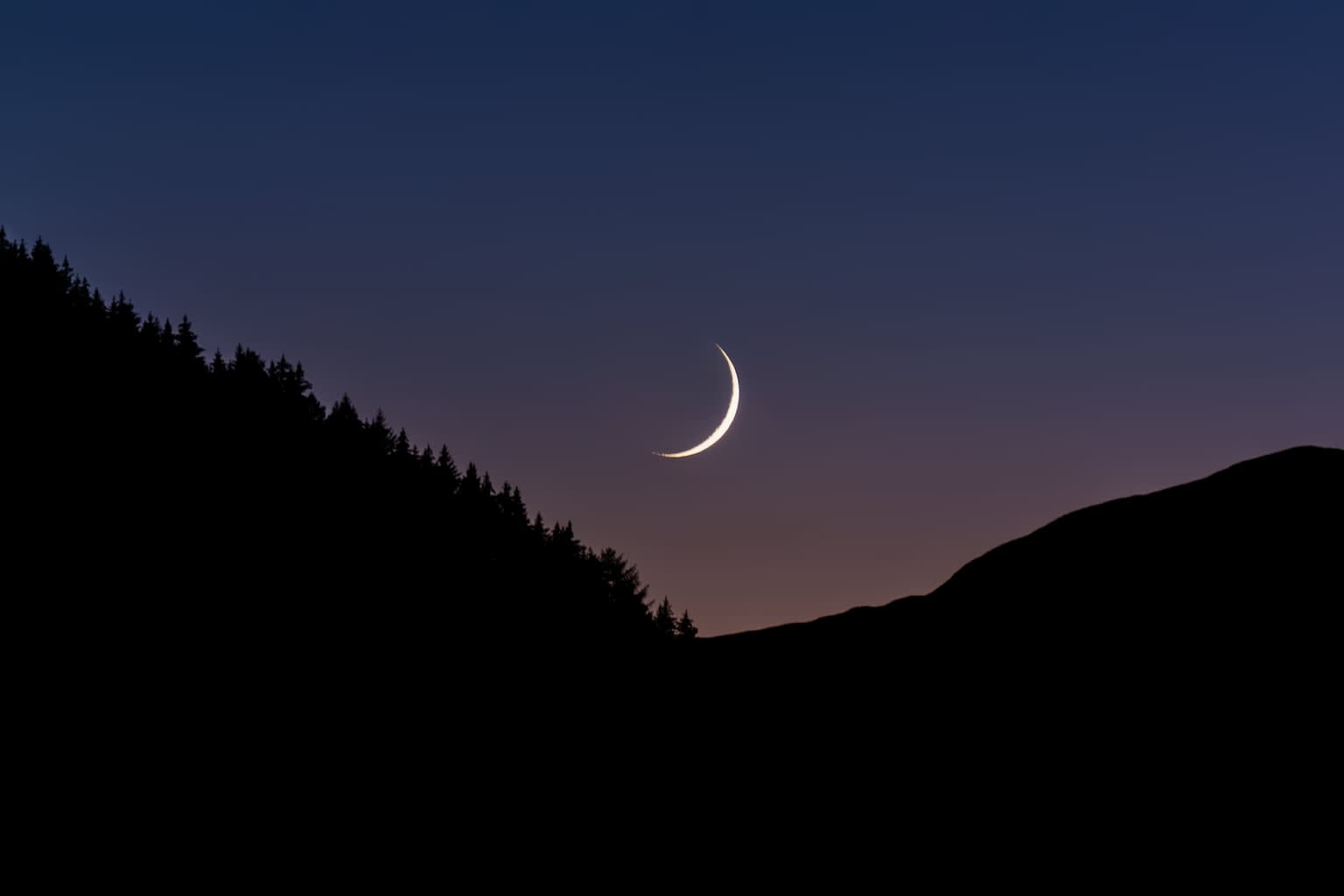 The moon setting over a mountain range at twilight.