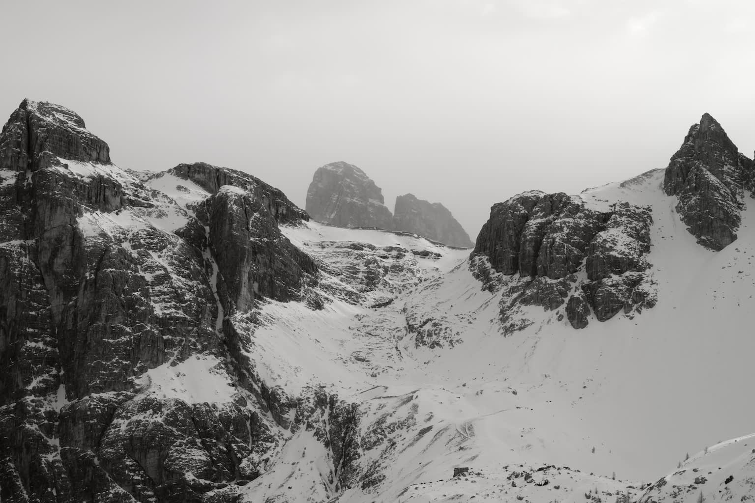 The Zwölferkofel mountain peeking behind another mountain range covered in snow and rendered in near-monochrome with a slight tint of red.