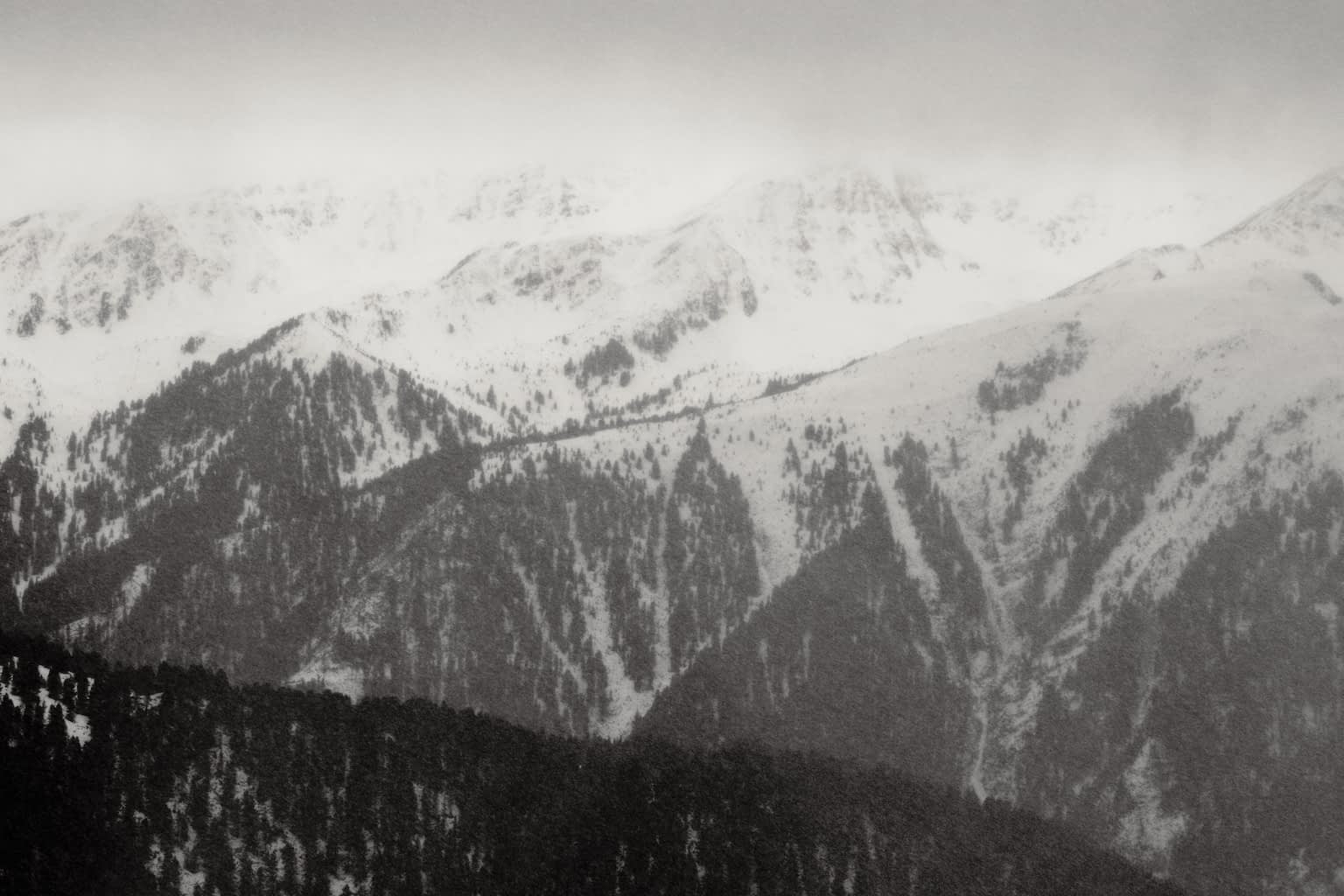 A near-monochrome image of the mountain Plose as seen from north-east through a snowstorm. The mountain peek Großer Gabler is hidden in clouds with the snowfall rendering the image fuzzy.