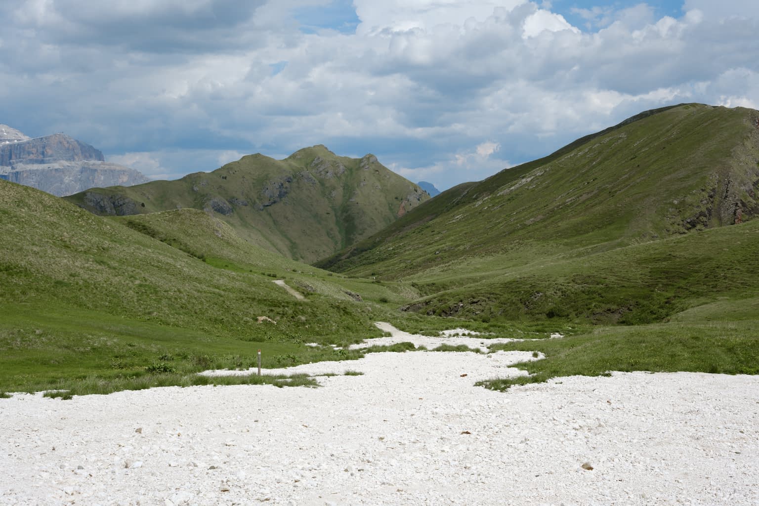 View of a mountainous panorama featuring the Ponjin Peak in the center with white stones in the foreground and a blue, cloudy sky in the background.